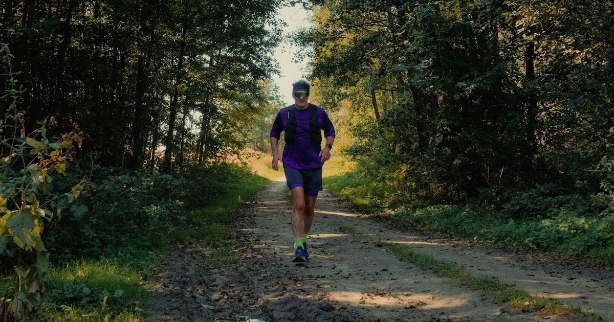 A man running on a dirt path through a sunlit forest