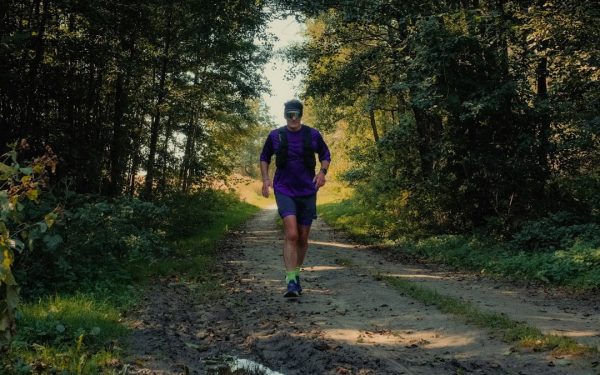 A man running on a dirt path through a sunlit forest