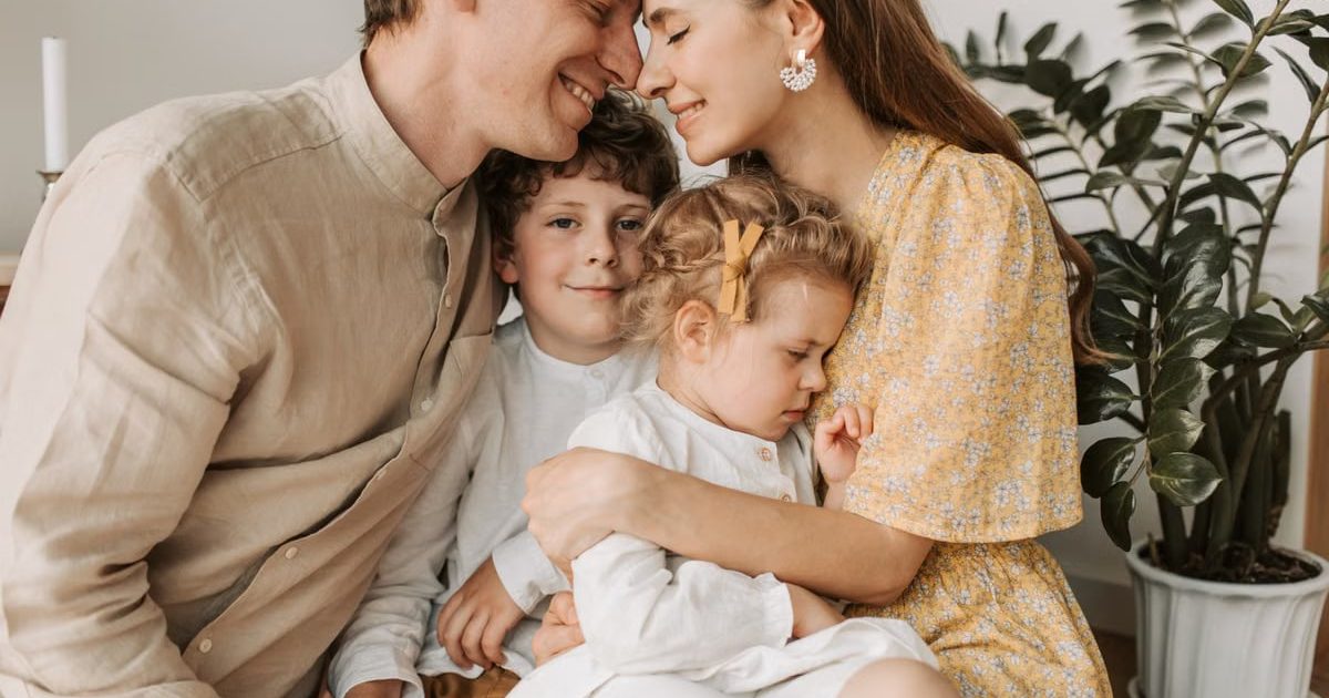 A loving family of four shares a tender moment in a cozy indoor setting, embracing and smiling.