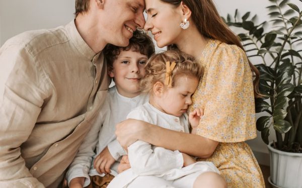 A loving family of four shares a tender moment in a cozy indoor setting, embracing and smiling.